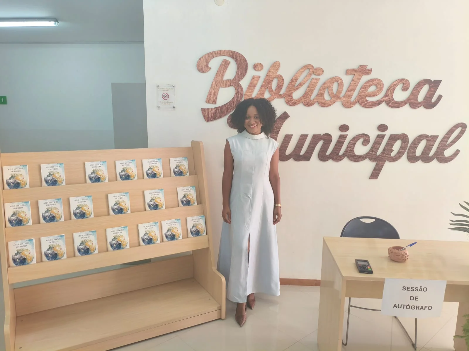 Alissa Mendes junto ao expositor com exemplares, na Biblioteca Municipal da Boavista