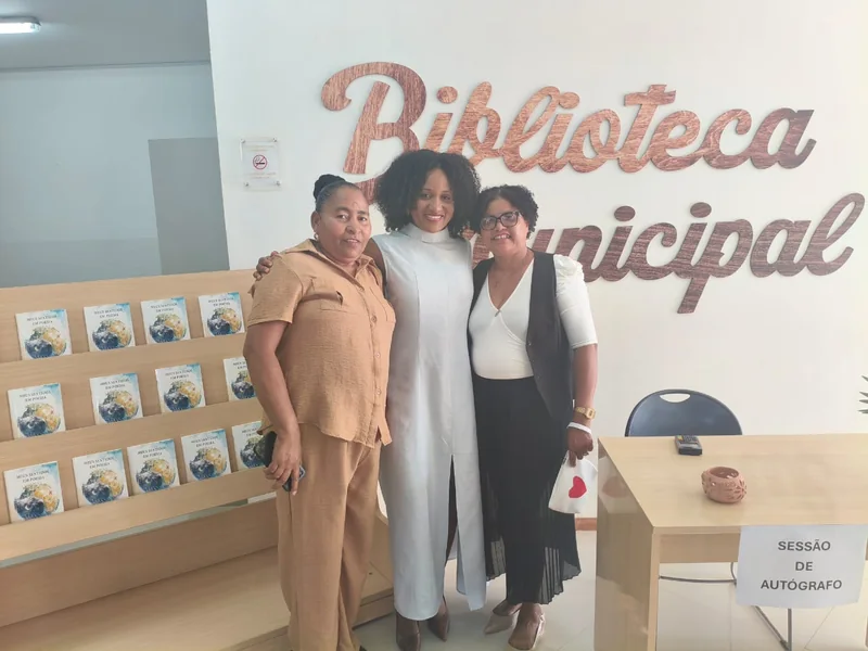 Alissa Mendes com duas leitoras junto ao expositor de livros